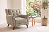 Comacchio armchair in light brown beside a pale oak side table in a bright garden room with ferns and an olive tree