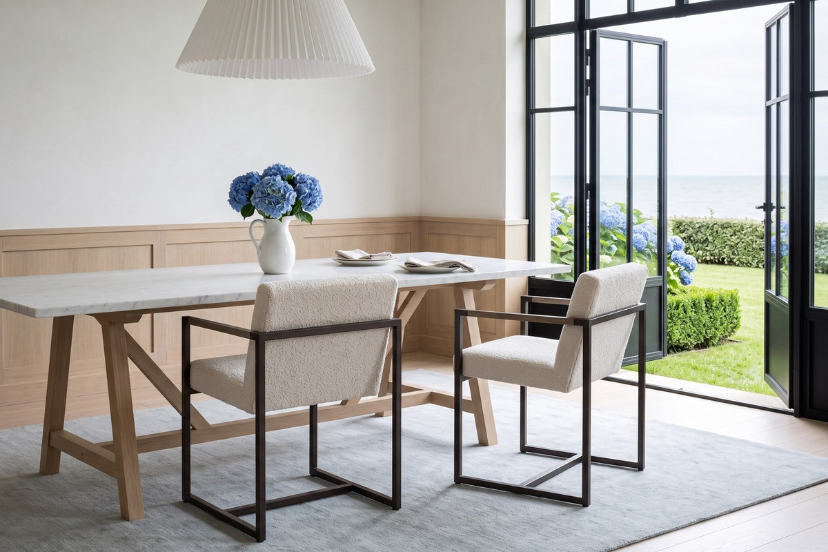 Two Coreglia dining armchairs in White seen from behind at a marble table on oak trestles in a Deauville seaside villa