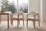 A pair of Corinaldo dining chairs pulled out from a white-oak table in a bright Vancouver dining room with cedar trees