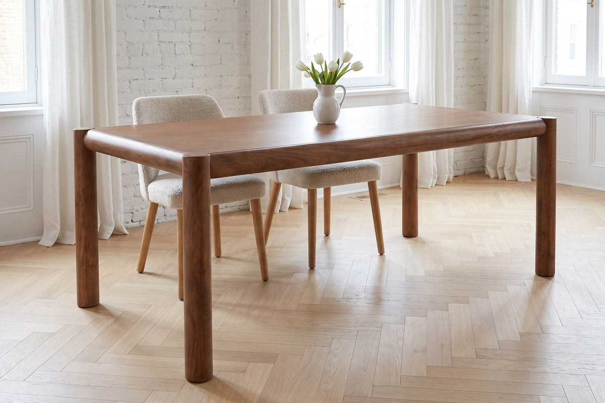 Corniglia dining table in walnut in a Montreal apartment with a whitewashed brick wall, two boucle chairs on the far side