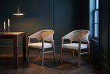 A pair of Cortina cane-back dining chairs in a dark green Toronto dining room at dusk beside a walnut table and a brass penda
