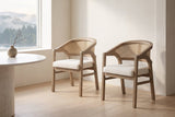 A pair of Cortina cane-back dining chairs in a bright Vancouver dining area with a round travertine table and a misty view