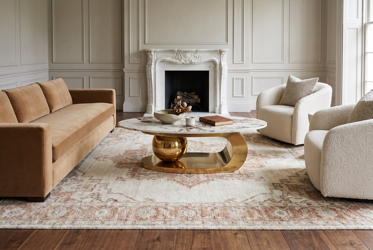 The Cosima coffee table on an ivory and rust rug between a camel velvet sofa and two ivory boucle armchairs, in a greige panelled drawing room with a carved white marble fireplace
