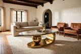 The Cosima coffee table on an ivory rug in front of a linen sofa and two cognac leather lounge chairs, in a plaster living room with a beamed ceiling and an arched doorway