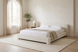 Cupello boucle bed made up with white linen in a bright bedroom with an arched window and an olive tree