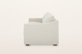 Cupramontana sofa in Beige, side view on a warm white studio backdrop: the arm top dips in a scoop and rises toward the back