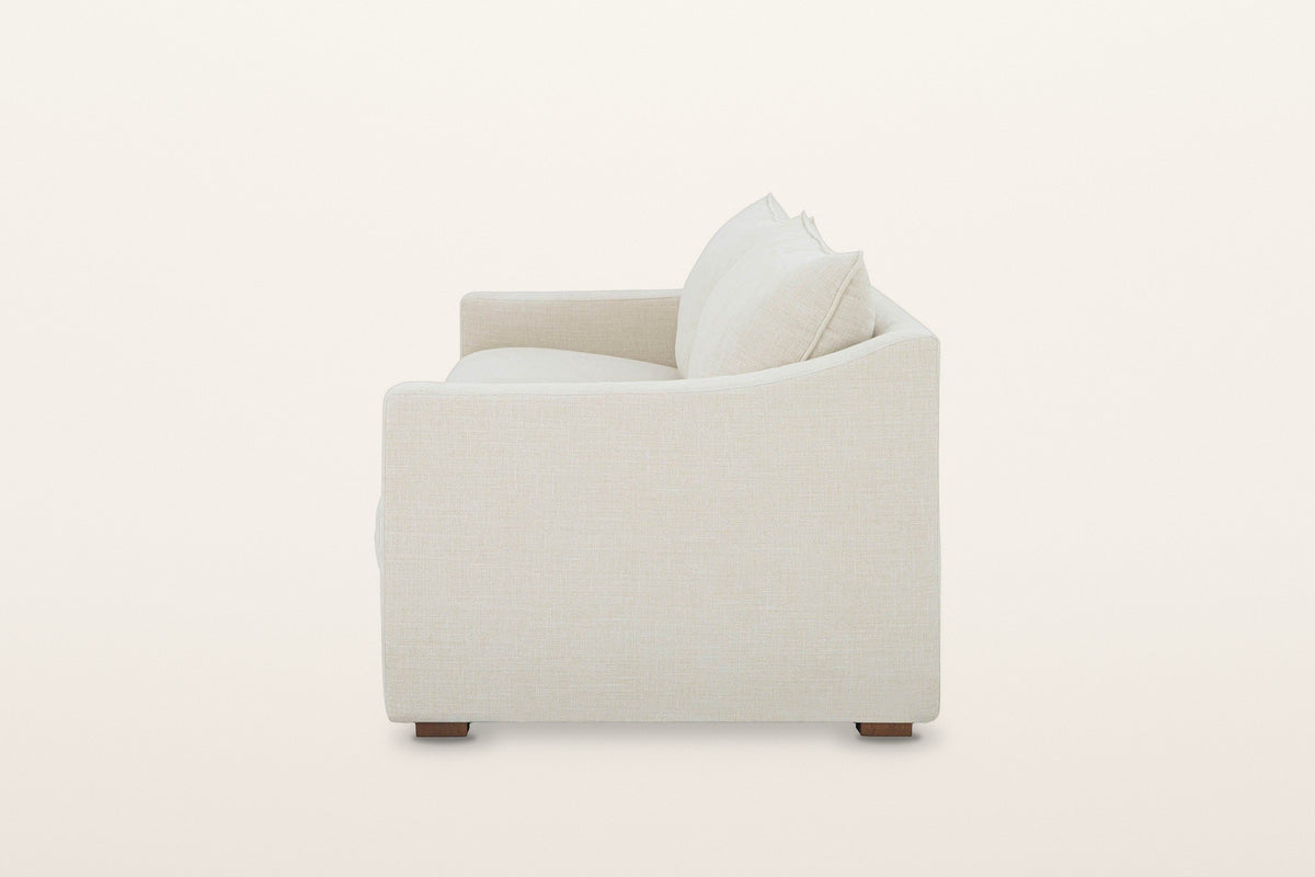 Cupramontana sofa in Beige, side view on a warm white studio backdrop: the arm top dips in a scoop and rises toward the back