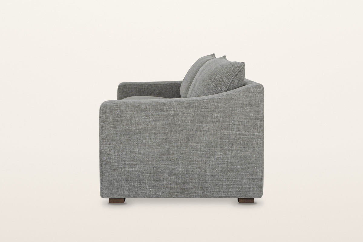 Cupramontana sofa in Grey, side view on a warm white studio backdrop: the arm top dips in a scoop and rises toward the back