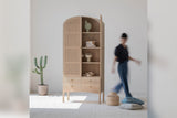 Dalton arched tall cabinet with one door open in a room, a person walking past for scale