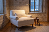 Dolceacqua chair in a stone-walled Quebec City reading corner on a winter evening, a brass floor lamp lit beside it