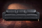 The Elodie sofa seen from the front on a dark walnut herringbone floor against a plaster wall, headrests down and footrests closed. Shown in Aged Slate, 3 seat.