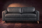 The Elodie loveseat seen from the front on a dark walnut herringbone floor against a plaster wall, headrests down and footrests closed. Shown in Aged Slate, Loveseat.