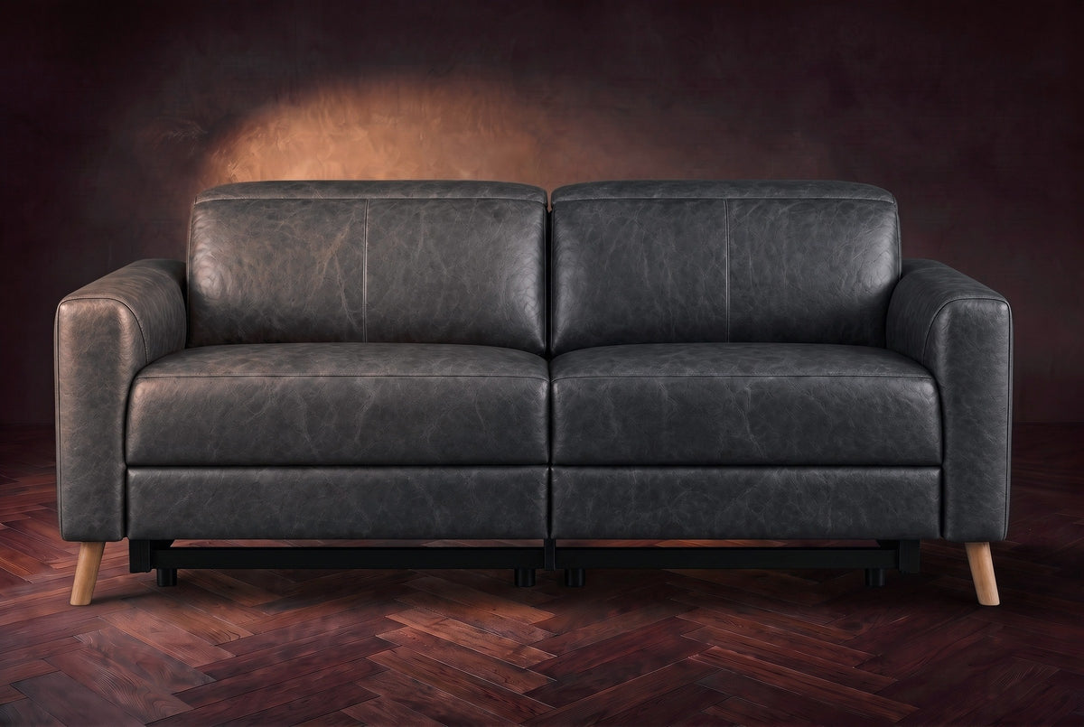 The Elodie loveseat seen from the front on a dark walnut herringbone floor against a plaster wall, headrests down and footrests closed. Shown in Aged Slate, Loveseat.
