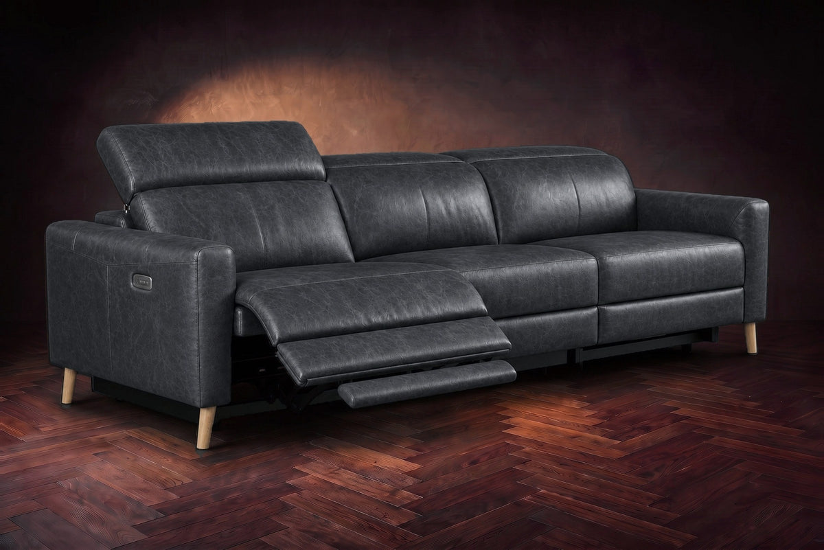 The Elodie sofa on a dark walnut herringbone floor, the left outer seat reclined with its footrest out and its headrest raised. Shown in Aged Slate, 3 seat.
