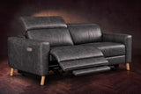 The Elodie loveseat on a dark walnut herringbone floor, the left seat reclined with its footrest out and its headrest raised. Shown in Aged Slate, Loveseat.