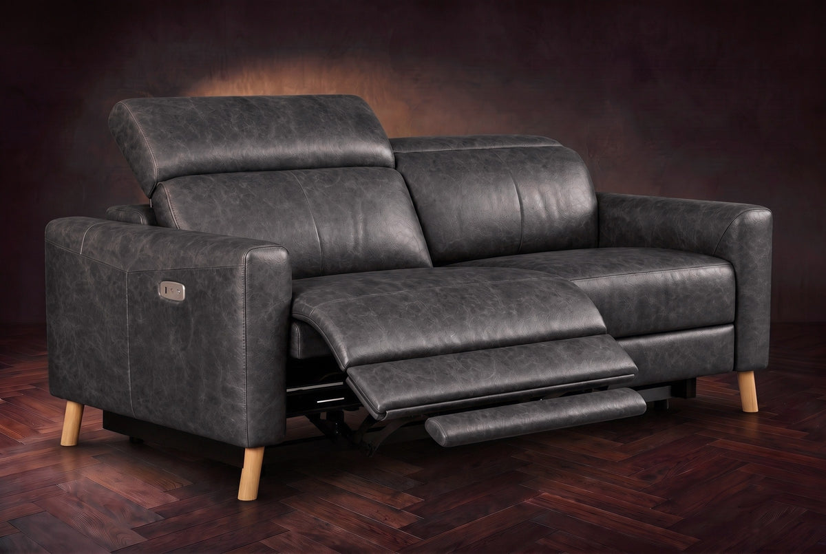The Elodie loveseat on a dark walnut herringbone floor, the left seat reclined with its footrest out and its headrest raised. Shown in Aged Slate, Loveseat.
