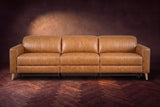 The Elodie sofa seen from the front on a dark walnut herringbone floor against a plaster wall, headrests down and footrests closed. Shown in Antiqued Caramel, 3 seat.