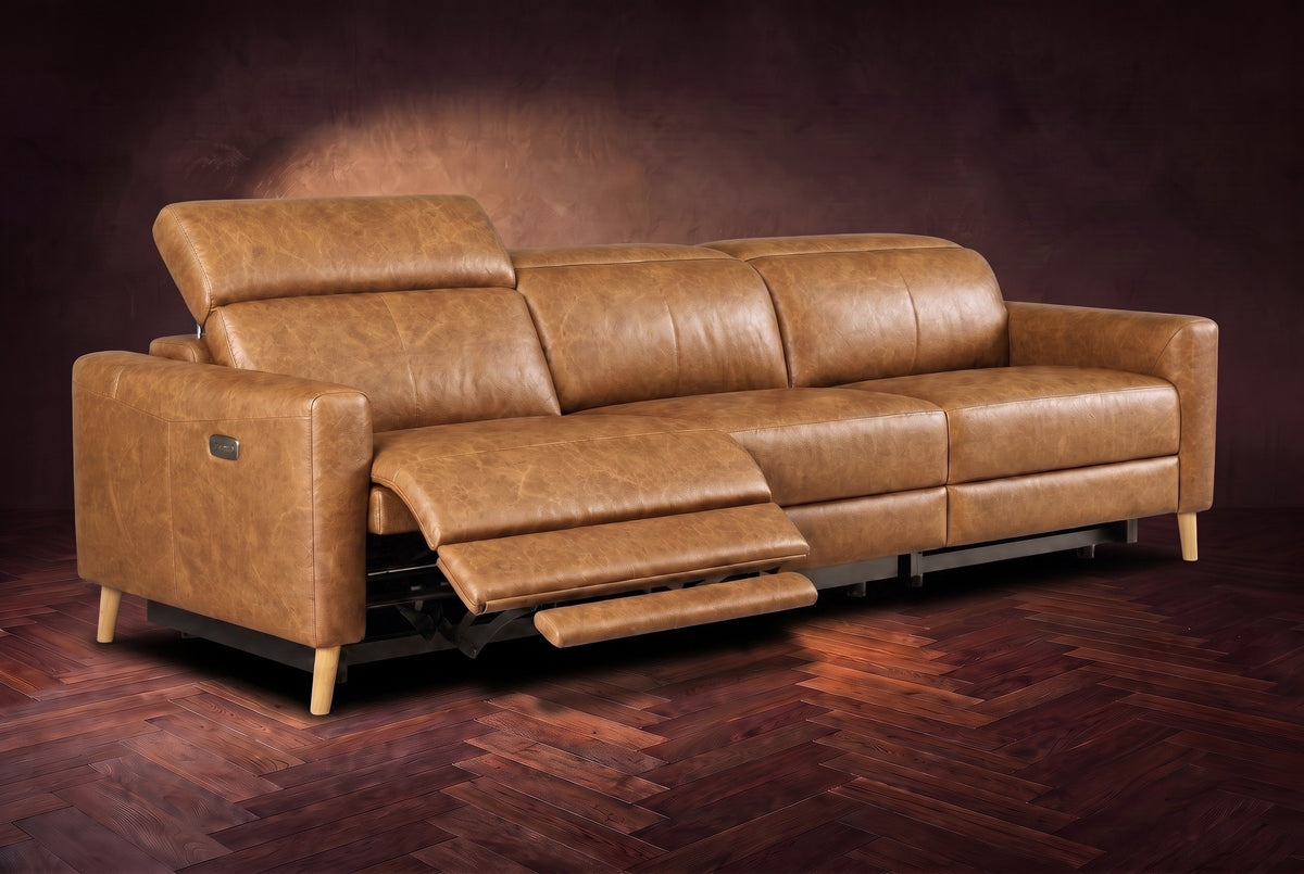 The Elodie sofa on a dark walnut herringbone floor, the left outer seat reclined with its footrest out and its headrest raised. Shown in Antiqued Caramel, 3 seat.