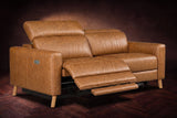 The Elodie loveseat on a dark walnut herringbone floor, the left seat reclined with its footrest out and its headrest raised. Shown in Antiqued Caramel, Loveseat.
