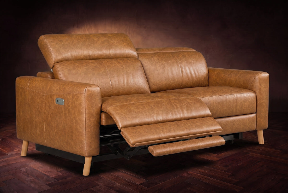 The Elodie loveseat on a dark walnut herringbone floor, the left seat reclined with its footrest out and its headrest raised. Shown in Antiqued Caramel, Loveseat.