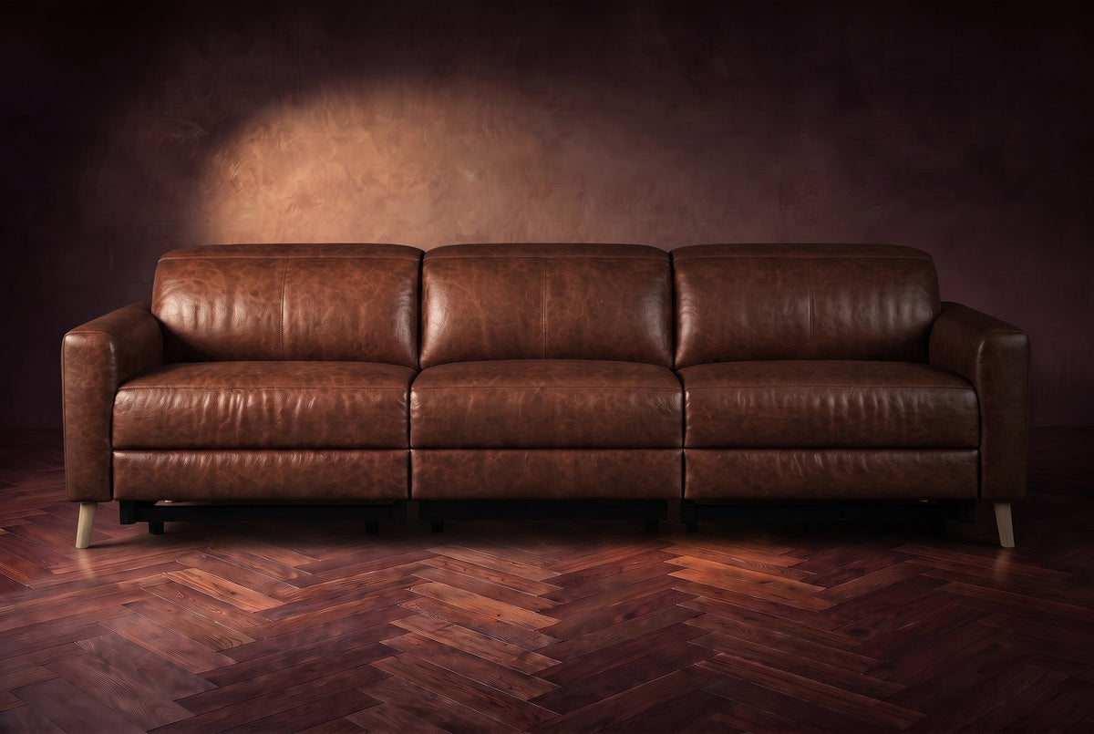 The Elodie sofa seen from the front on a dark walnut herringbone floor against a plaster wall, headrests down and footrests closed. Shown in Burnished Chestnut, 3 seat.