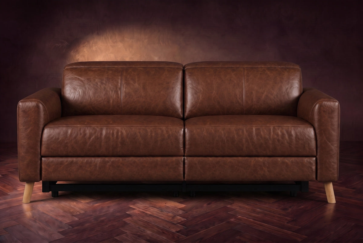 The Elodie loveseat seen from the front on a dark walnut herringbone floor against a plaster wall, headrests down and footrests closed. Shown in Burnished Chestnut, Loveseat.