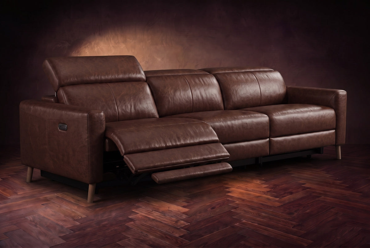 The Elodie sofa on a dark walnut herringbone floor, the left outer seat reclined with its footrest out and its headrest raised. Shown in Burnished Chestnut, 3 seat.