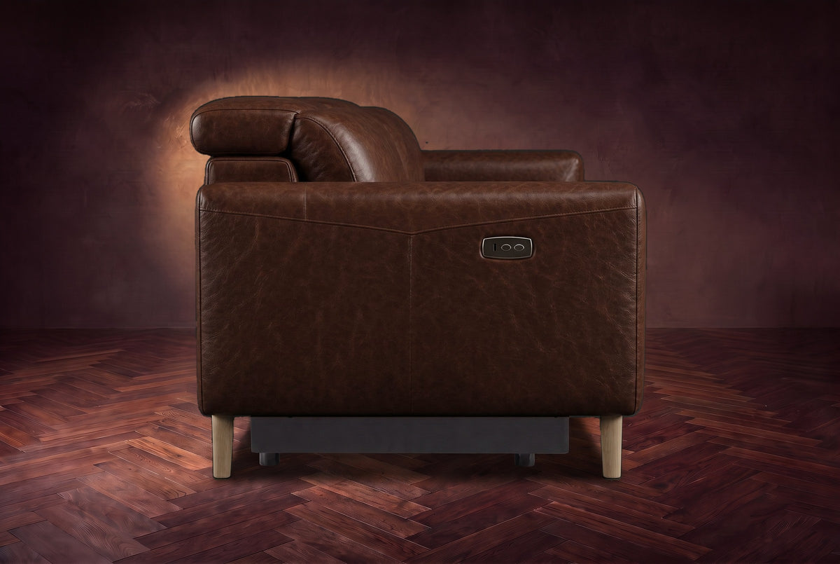 The left end of the Elodie sofa seen from the side on a dark walnut herringbone floor, the control panel on the arm and the headrest raised. Shown in Burnished Chestnut, 3 seat.