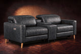 The Elodie sofa with console in Aged Slate distressed full leather on a dark herringbone floor, headrests down and footrests closed.