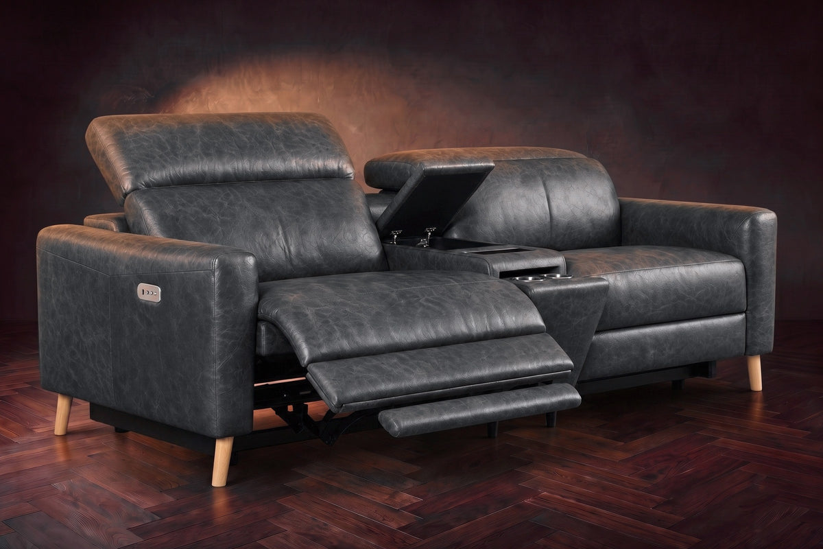 The Elodie sofa with console in Aged Slate distressed full leather on a dark herringbone floor, the left seat reclined with its two-part footrest out and its headrest raised, the console lid open.