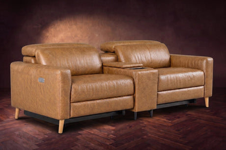 The Elodie sofa with console in Antiqued Caramel distressed full leather on a dark herringbone floor, headrests down and footrests closed.