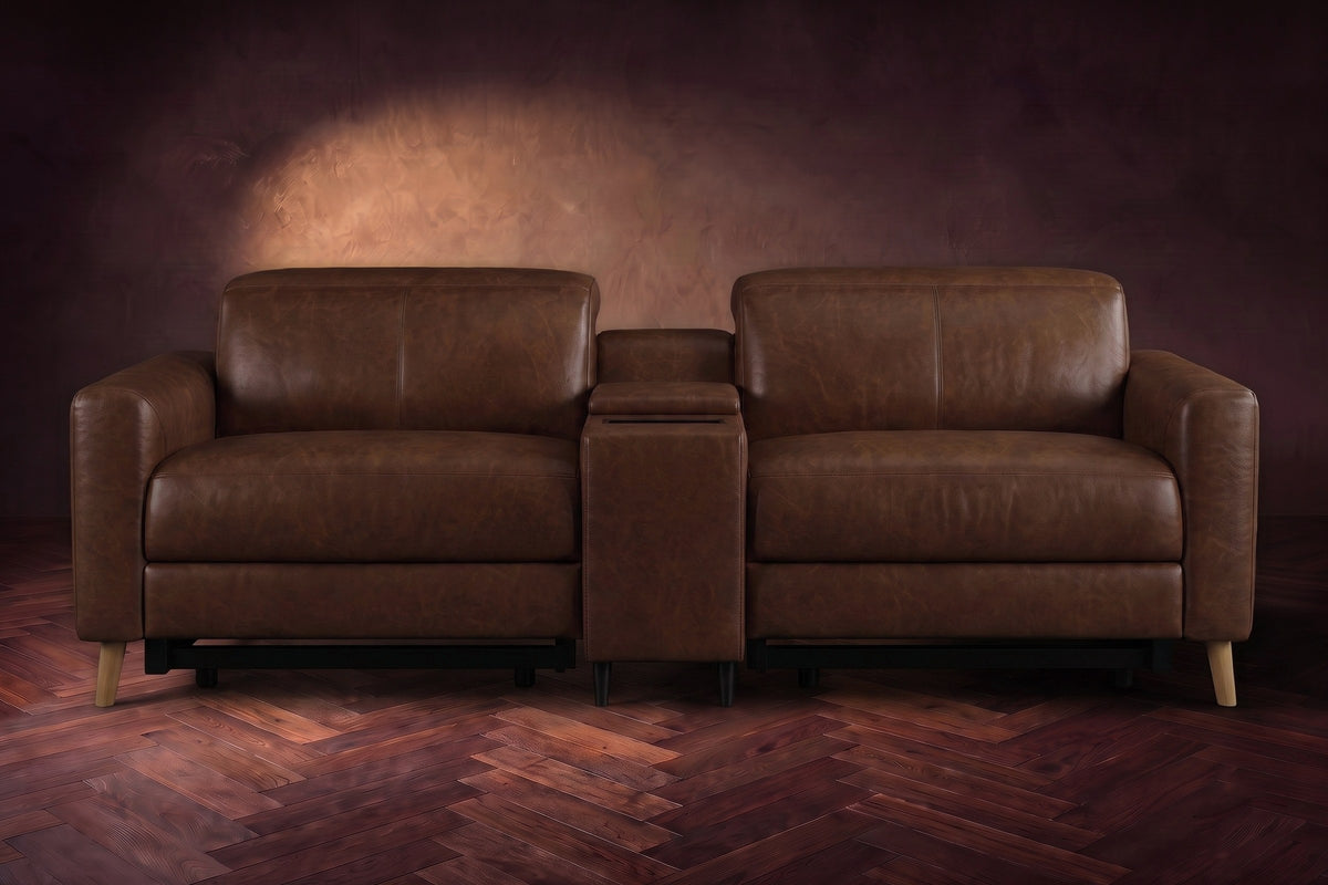 The Elodie sofa with console seen from the front in Burnished Chestnut distressed full leather on a dark herringbone floor, headrests down and footrests closed.