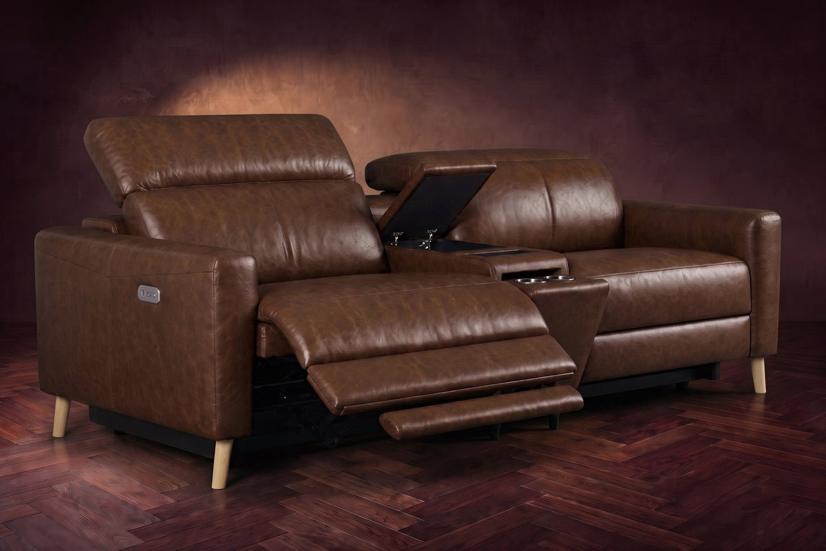 The Elodie sofa with console in Burnished Chestnut distressed full leather on a dark herringbone floor, the left seat reclined with its two-part footrest out and its headrest raised, the console lid open.