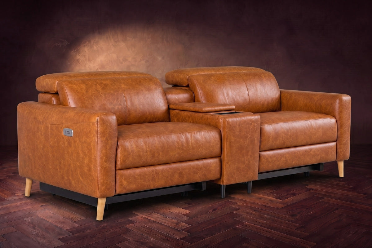 The Elodie sofa with console in Tuscan Cognac distressed full leather on a dark herringbone floor, headrests down and footrests closed.