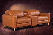 The Elodie sofa with console in Tuscan Cognac distressed full leather on a dark herringbone floor, headrests down and footrests closed.