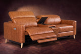 The Elodie sofa with console in Tuscan Cognac distressed full leather on a dark herringbone floor, the left seat reclined with its two-part footrest out and its headrest raised, the console lid open.