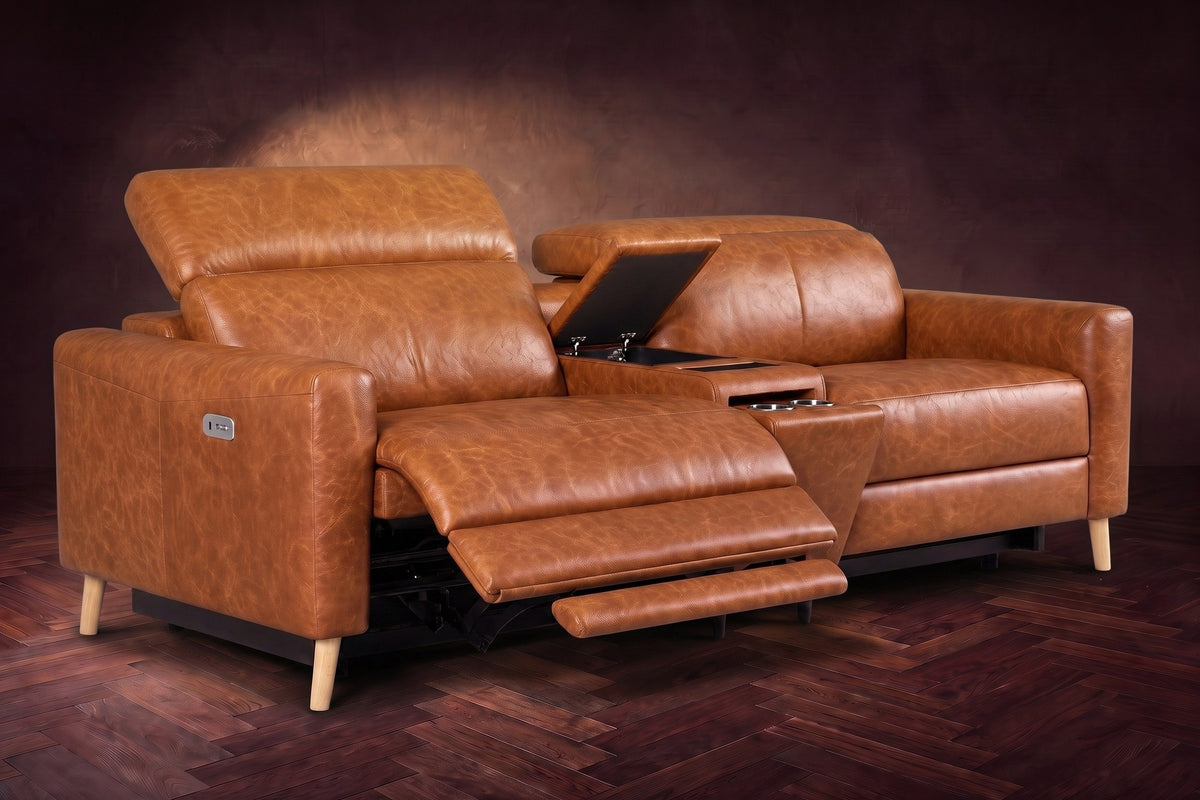 The Elodie sofa with console in Tuscan Cognac distressed full leather on a dark herringbone floor, the left seat reclined with its two-part footrest out and its headrest raised, the console lid open.