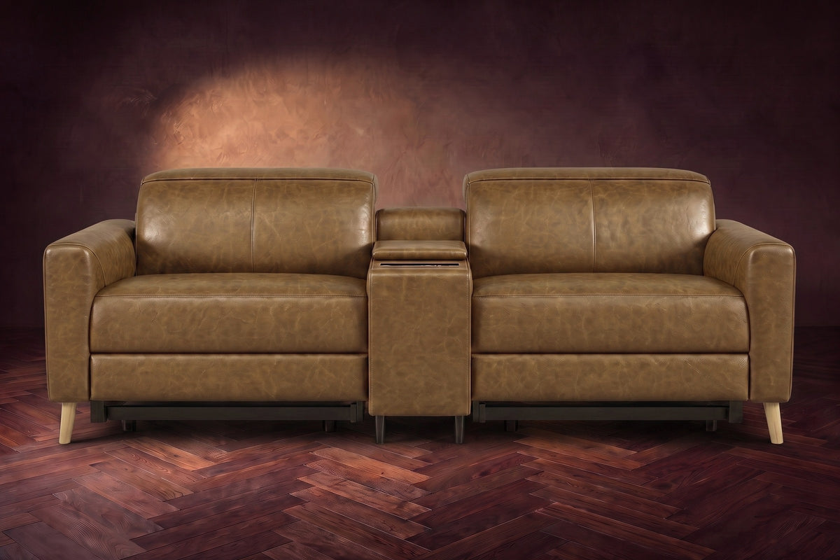 The Elodie sofa with console seen from the front in Weathered Saddle distressed full leather on a dark herringbone floor, headrests down and footrests closed.