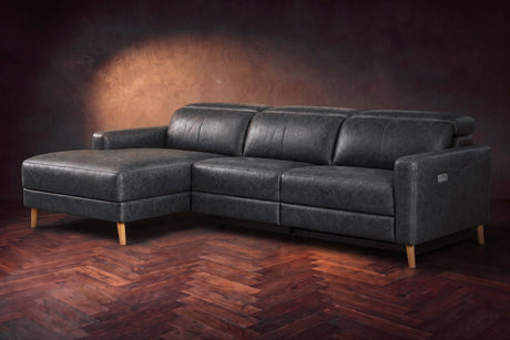 The Elodie sectional on a dark walnut herringbone floor in front of a warm plaster wall, three-quarter view, headrests down and the footrest closed. Shown in Aged Slate, Left chaise.