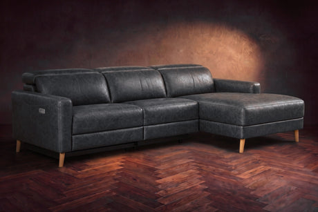 The Elodie sectional on a dark walnut herringbone floor in front of a warm plaster wall, three-quarter view, headrests down and the footrest closed. Shown in Aged Slate, Right chaise.