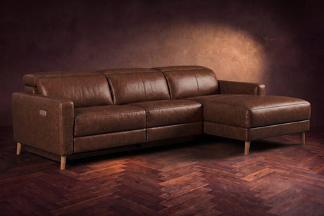 The Elodie sectional on a dark walnut herringbone floor in front of a warm plaster wall, three-quarter view, headrests down and the footrest closed. Shown in Burnished Chestnut, Right chaise.