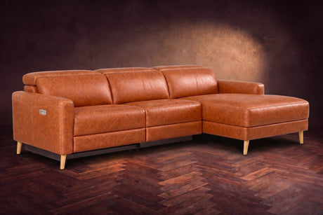 The Elodie sectional on a dark walnut herringbone floor in front of a warm plaster wall, three-quarter view, headrests down and the footrest closed. Shown in Tuscan Cognac, Right chaise.
