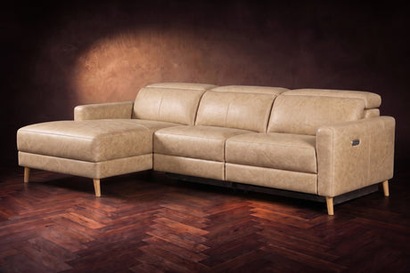 The Elodie sectional on a dark walnut herringbone floor in front of a warm plaster wall, three-quarter view, headrests down and the footrest closed. Shown in Washed Sand, Left chaise.