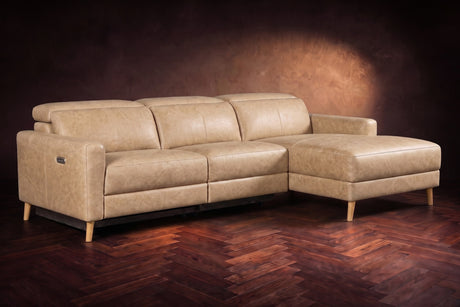 The Elodie sectional on a dark walnut herringbone floor in front of a warm plaster wall, three-quarter view, headrests down and the footrest closed. Shown in Washed Sand, Right chaise.