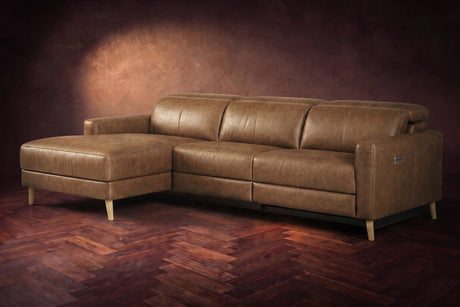 The Elodie sectional on a dark walnut herringbone floor in front of a warm plaster wall, three-quarter view, headrests down and the footrest closed. Shown in Weathered Saddle, Left chaise.