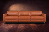 The Elodie sofa seen from the front on a dark walnut herringbone floor against a plaster wall, headrests down and footrests closed. Shown in Tuscan Cognac, 3 seat.