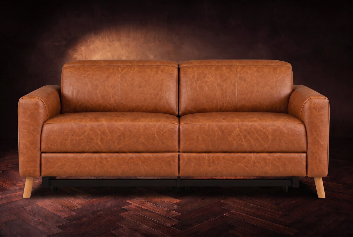 The Elodie loveseat seen from the front on a dark walnut herringbone floor against a plaster wall, headrests down and footrests closed. Shown in Tuscan Cognac, Loveseat.