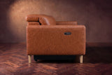 The left end of the Elodie sofa seen from the side on a dark walnut herringbone floor, the control panel on the arm and the headrest raised. Shown in Tuscan Cognac, 3 seat.