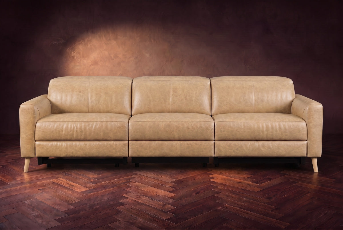 The Elodie sofa seen from the front on a dark walnut herringbone floor against a plaster wall, headrests down and footrests closed. Shown in Washed Sand, 3 seat.