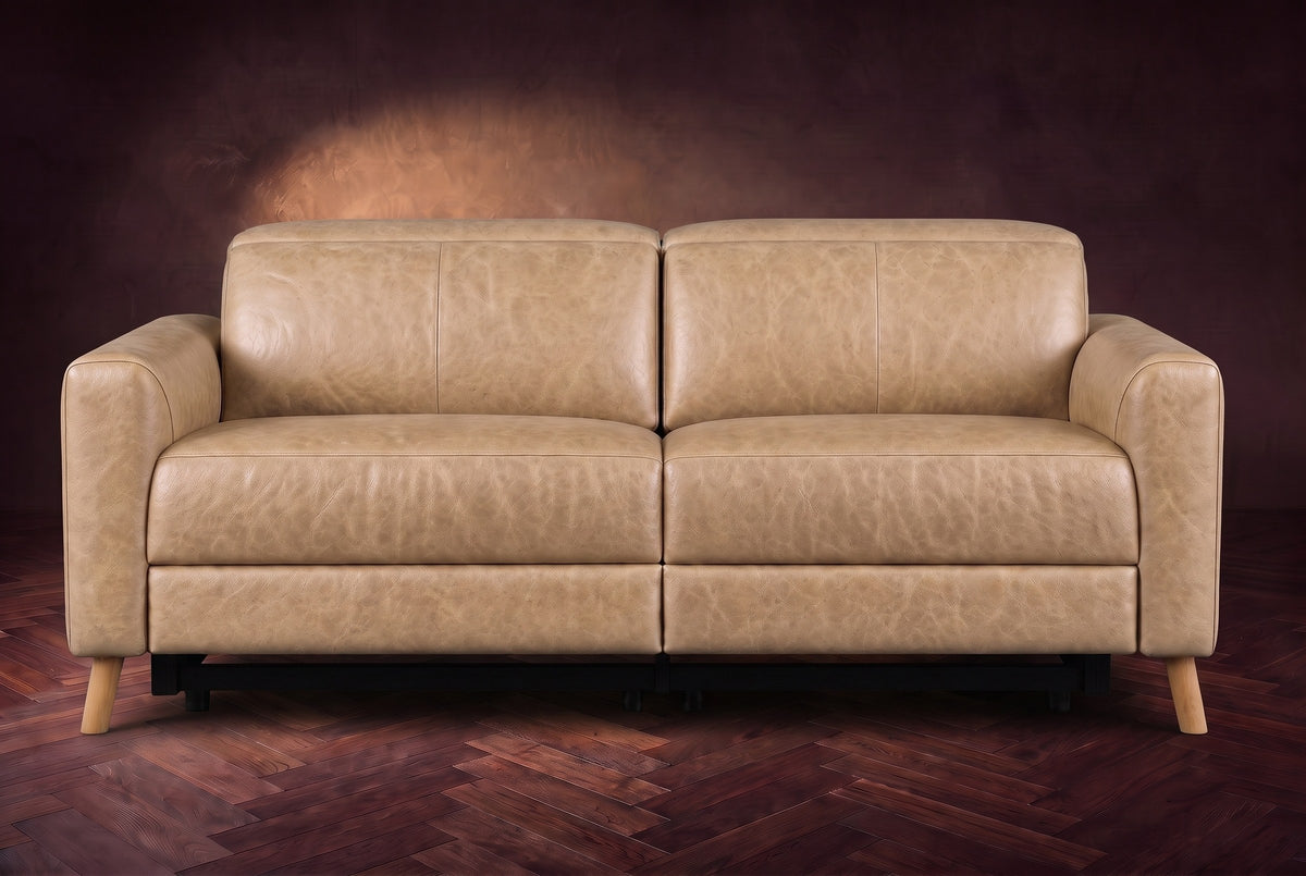 The Elodie loveseat seen from the front on a dark walnut herringbone floor against a plaster wall, headrests down and footrests closed. Shown in Washed Sand, Loveseat.